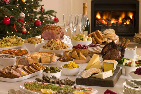 Mesa cheia de almoço buffet no Boxing Day, árvore de Natal e lareira. Peru, champanhe, queijo