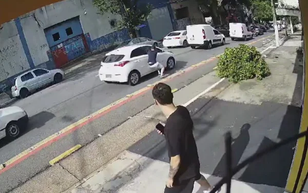 Imagem colorida mostra bandido quebrando vidro de carro com o cotovelo para roubar celular do motorista em São Paulo - Metrópoles