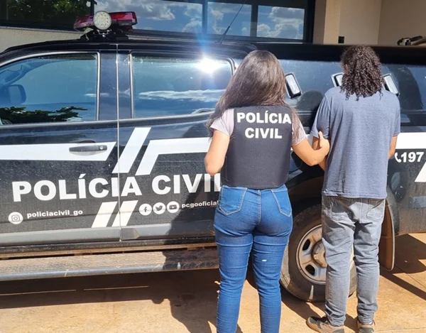 Imagem colorida de homem preso na frente de viatura em Goiás