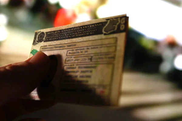 Imagem colorida de uma mão segurando uma carteira nacional de habilitação. Os dados estão borrados