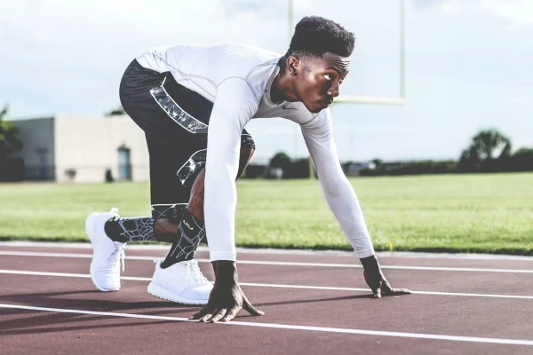 Foto colorida de homem vestindo sueter branco e shorts pretos prestes a correr - Metrópoles