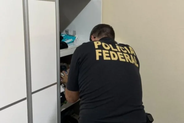 Imagem colorida de policial federal de costas abrindo gaveta. Metrópoles