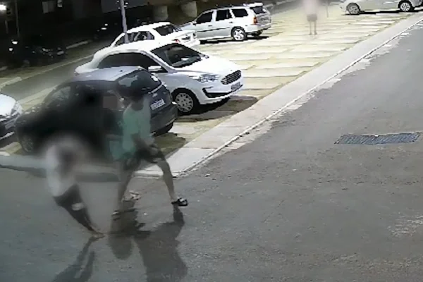 Imagem colorida de um homem agredindo um adolescente com um soco no rosto. Outra adolescente está ao lado na cena. No fundo, há carros e prédios