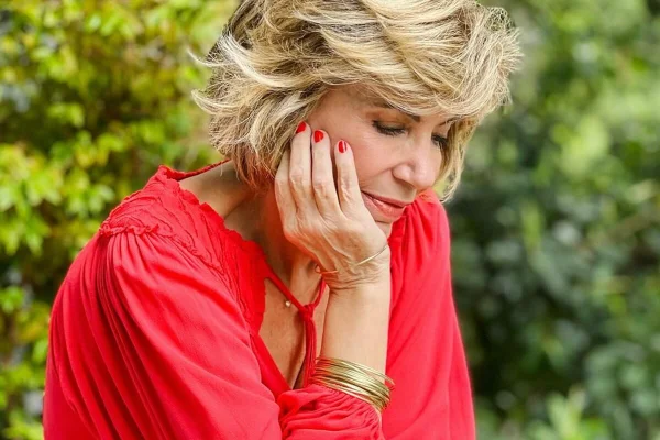 Silvia Poppovic posa,de cabeça baixa, de blusa vermelha e com a mão no queixo - Metrópoles