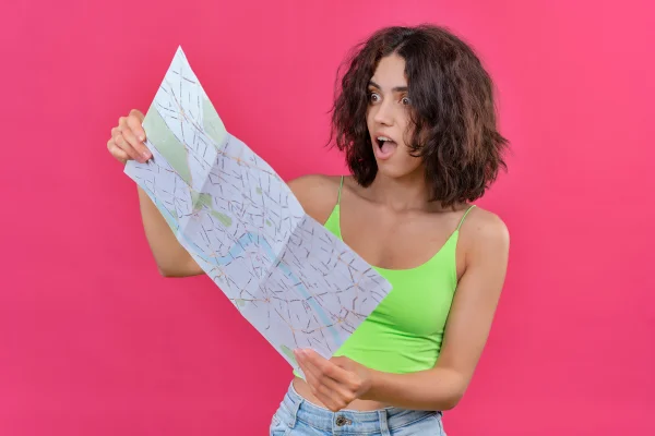 Foto colorida de mulher olhando mapa com expressão de surpresa
