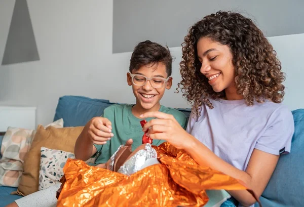 duas crianças abrem um ovo de páscoa. a menina aparenta ser mais velha que o garoto