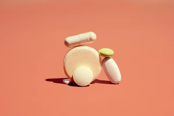 Foto mostra pílulas e suplementos empilhados em fundo cor terroso