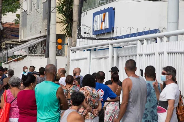 Na imagem colorida, há pessoas de costas olhando para uma residência com faixada indicando a empresa caixa