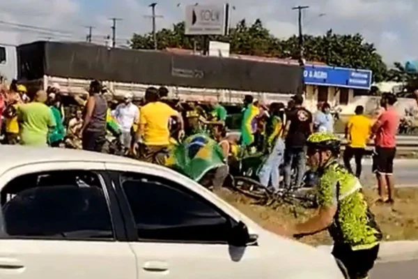 foto colorida de ciclista na frente de carro em manifestação de bolsonaristas