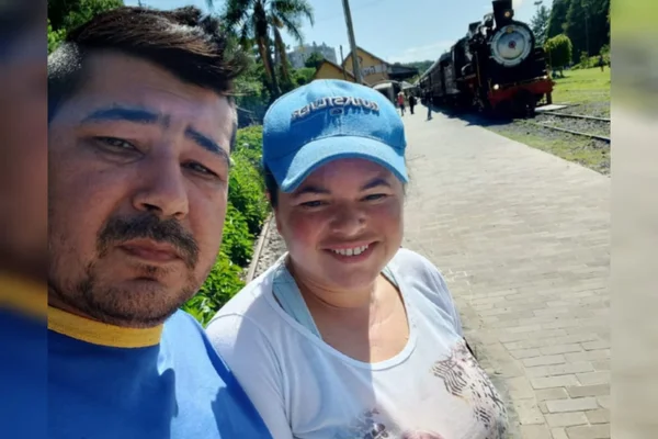 Imagem mostra homem e mulher de boné em primeiro plano com uma estação de trem ao fundo. Ele é Jair dos Santos, que tem a doença de Fabry