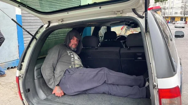 Em foto colorida homem com moletom, com capuz sobre a cabeça, dentro de "chiqueiro" de viatura policial; ele matou um morador de rua na zona leste de São Paulo - Metrópoles