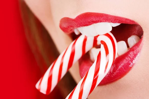 Foto colorida em close de mulher de batom vermelho com bengala doce na boca - Metrópoles