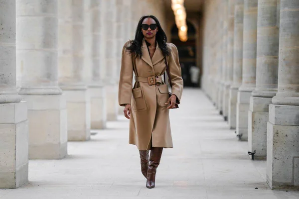 Mulher negra usando trench coat marrom claro com ombreiras e bota marrom over the knee