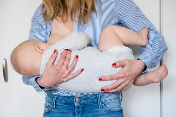 mulher de camisa azul e calça jeans amamentando um bebê