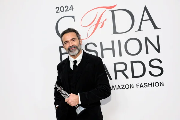 A imagems mostra o designer Daniel Roseberry em frente à tela com a logo do CFDA Awards