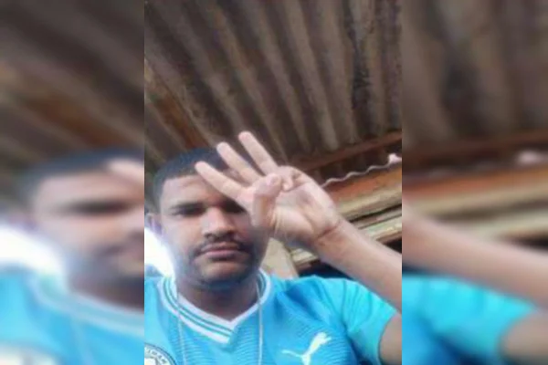 Imagem colorida de homem negro com blusa azul do Manchester City fazendo número 3 na mão, sinal do PCC