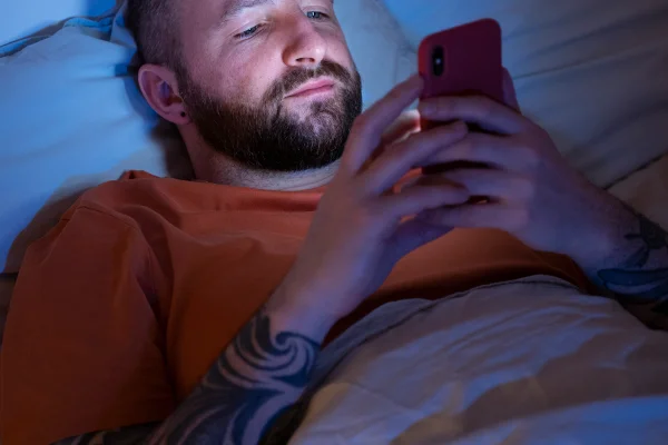 Imagem colorida de homem deitado na cama com o celular ligado - Metrópoles