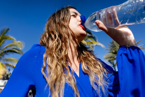Foto colorida de mulher de casaco azul tomando água - Metrópoles