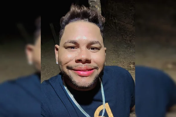 Imagem colorida de um homem negro, de cabelo preto curto, camiseta preta e corrente prata