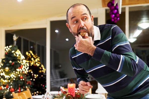 Foto colorida de homem pegando escondido o pedaço de alguma comida na ceia de natal - Metrópoles