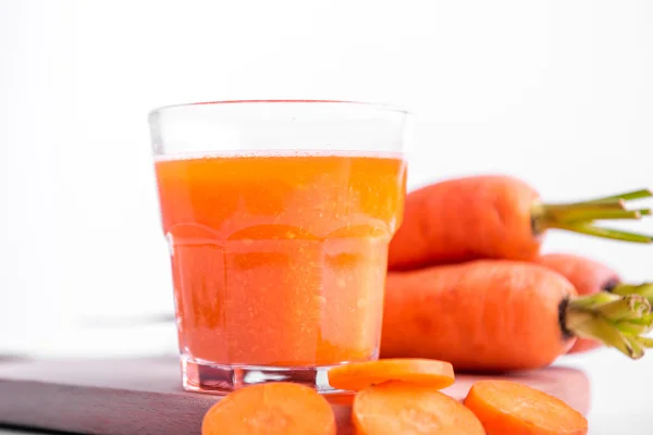 Imagem mostra copo transparente com suco laranja e pedaços de cenoura - Metrópoles
