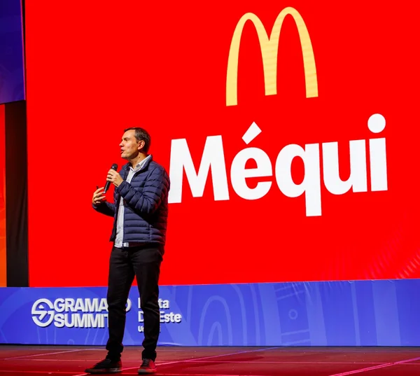 Fotografia colorida mostrando homem palestrando com a marca do McDonald's atrás em um telão-Metrópoles