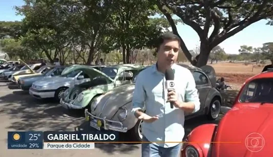 Na imagem, homem segura microfone enquanto apresenta uma reportagem usando uma camisa azul - Metrópoles