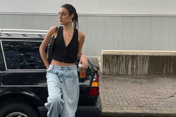 Influencer posa encostada em carro com colete preto e calça jeans de cintura baixa - Metrópoles