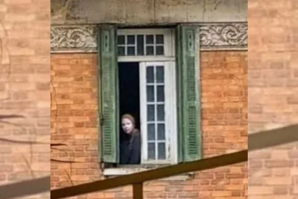 Conhecida como Mulher da Casa Abandonada, brasileira foragida do FBI aparece em janela de casarão desativado em São Paulo. Ela tem o rosto coberto por uma camada de pomada ou pó branco - Metrópoles
