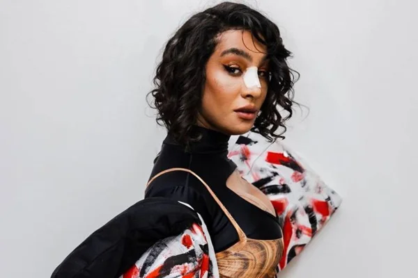 Imagem colorida mostra a cantora Linn da Quebrada, de lado, olhando para a câmera, vestida com uma camiseta preta de manda comprida e segurando acessórios nas cores branca, vermelha e preta - Metrópoles
