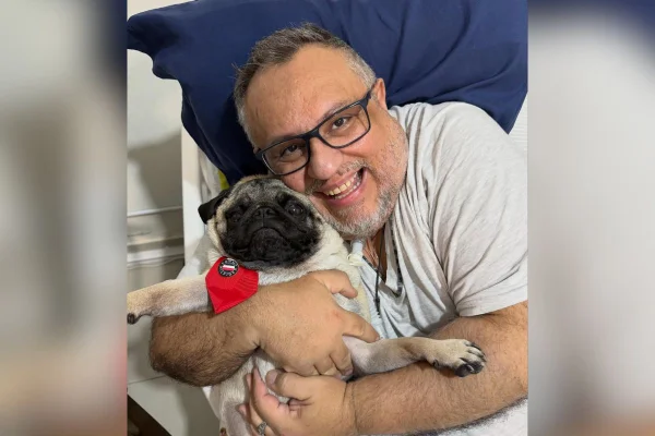 Imagem colorida mostra padre abraçado a um cachorro da raça pug - Metrópoles