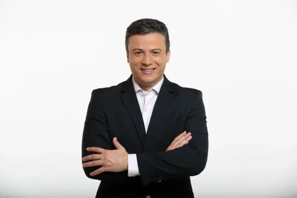Lucílio Macedo, repórter do SBT posa, de terno e sorridente, de braços cruzados - Metrópoles