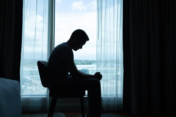 Homem solitário e triste sentado sozinho em um quarto escuro. Depressão. Metrópoles
