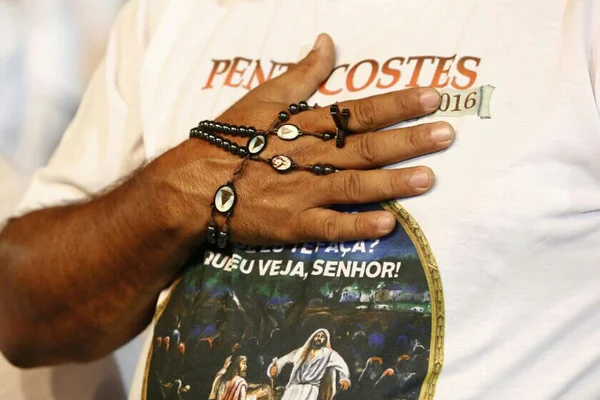 Mulher de camisa branca com terço na mão - Metrópoles