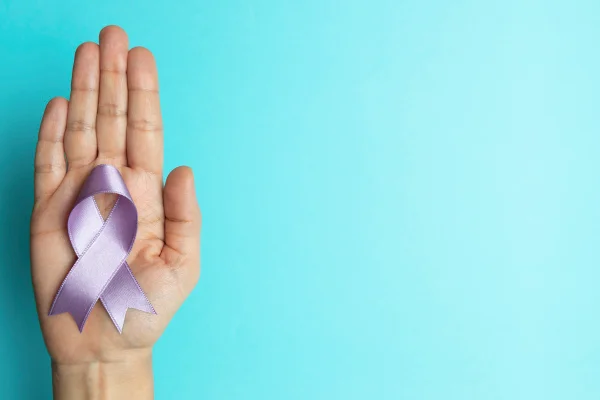 Foto de uma mão segurando uma fita lilás para representar o cuidado aos pacientes com lúpus - Metrópoles