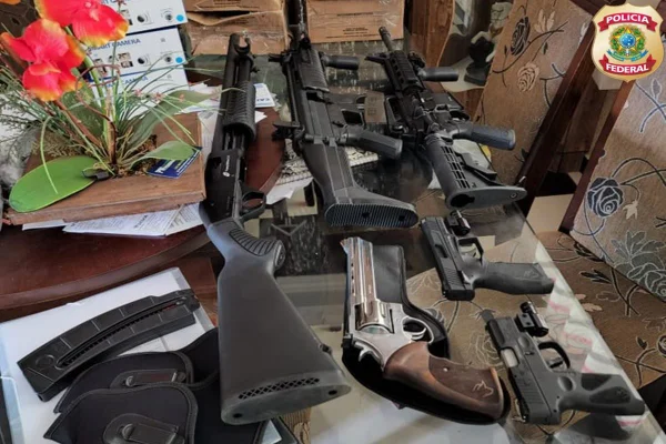 Carabina, pistola, espingarda e outras armas dispostas numa mesa