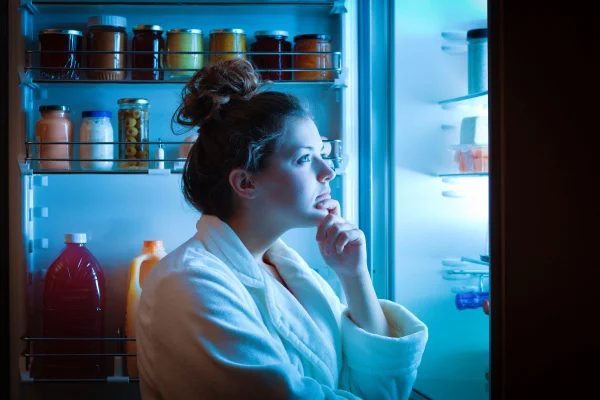 foto colorida mulher olhando para a geladeira para escolher o lanche noturno