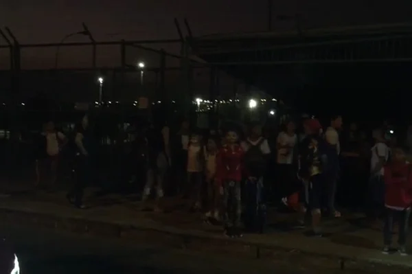 Crianças em calçada, em frente a grade, à noite