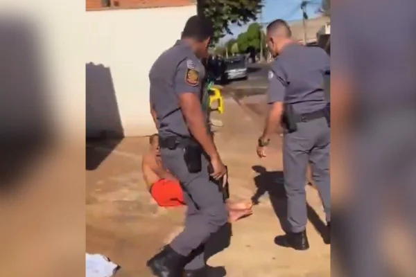 Imagem colorida mostra dois policiais olhando para homem caído no chão após levar tiro na perna - Metrópoles