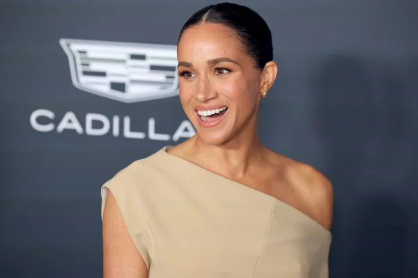Megan Markle, mulher negra com cabelo predo em um coque, vestido claro e sorriso no rosto