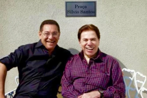 foto colorida de Jassa e Silvio Santos sentados em banco branco sorrindo - metrópoles