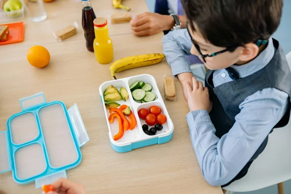 Foto colorida de criança comendo comida saudável da lancheira - Nutricionista infantil lista melhores alimentos para ter na lancheira - Metrópoles