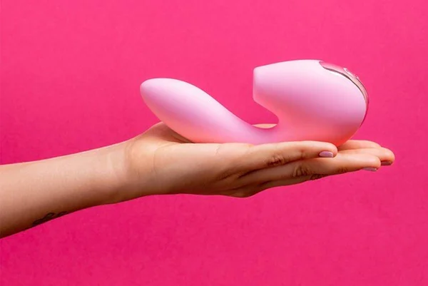 Mão feminina segurando um vibrador rosa em um fundo rosa mais escuro