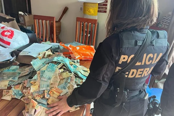 Imagem mosra agente da Polícia Federal perto de dinheiro capturado - Metrópoles