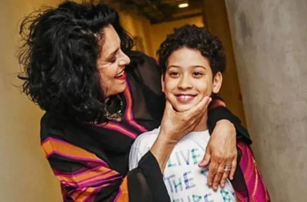 Gal Costa e o filho Gabriel. Ela tem o cabelo preto, está de roupa preto e é branca. Ele veste uma camisa branca, é branco e tem o cabelo preto - Metrópoles
