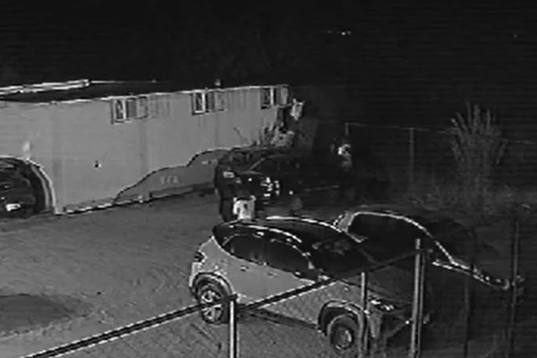 Imagem em preto e branco de jovens brincando no estacionamento de uma escola, com carros ao redor