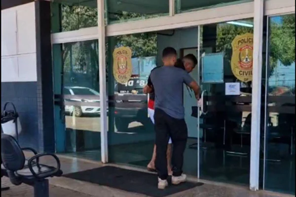 Foto colorida de policial de roupas casuais levando suspeito para delegacia