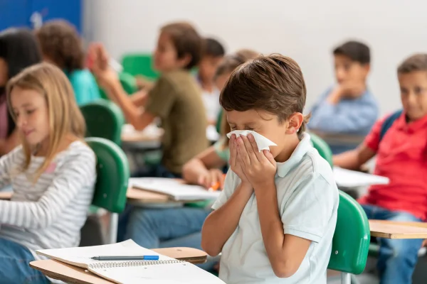 Retrato de um menino doente na escola assoando o nariz na aula - conceitos de estilo de vida