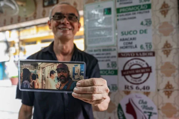 homem mostrando foto de cena do filme O Agente Secreto