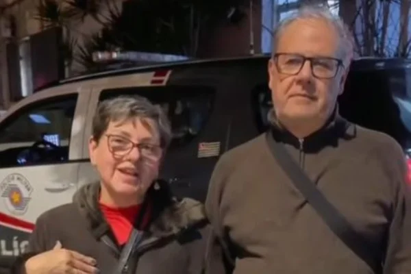Imagem colorida de um casal em frente a uma viatura de Polícia. Metrópoles
